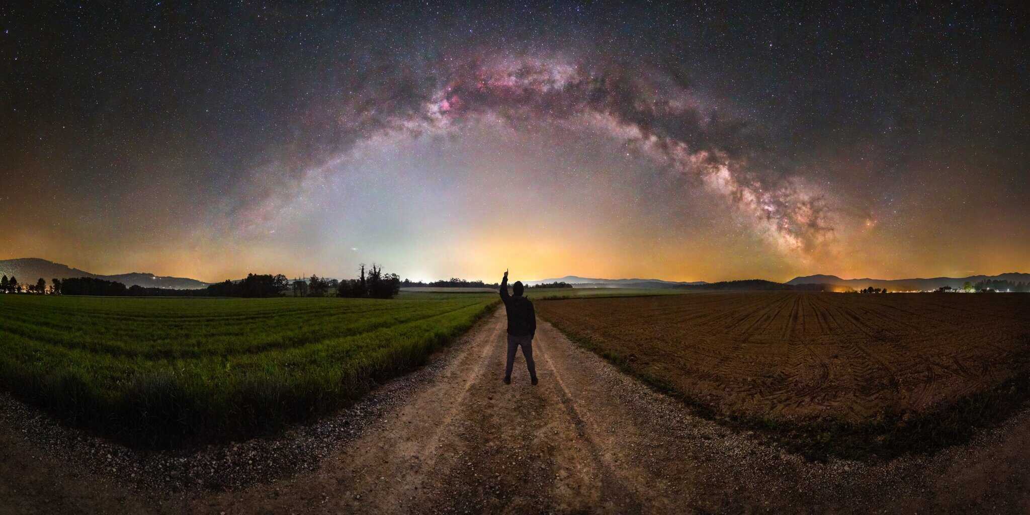 Between the Worlds by Uros Fink, a Milky Way arch over a landscape with a self-portrait