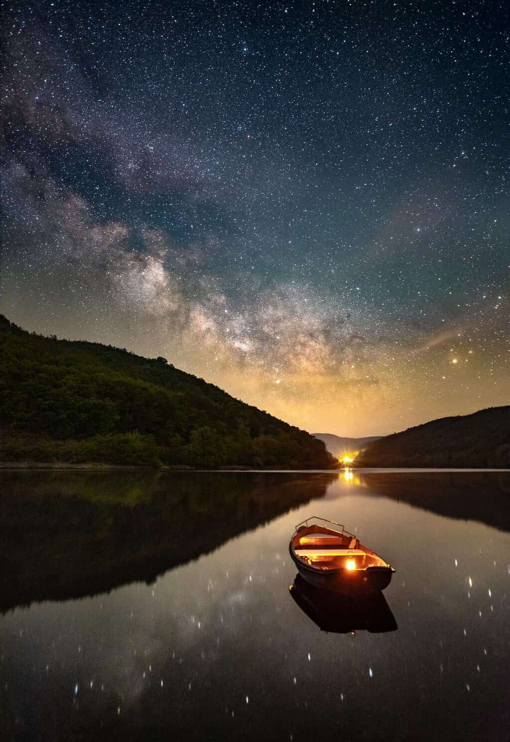 Milky Way reflected in a calm lake with a glowing boat by Evgeni Tcherkasski