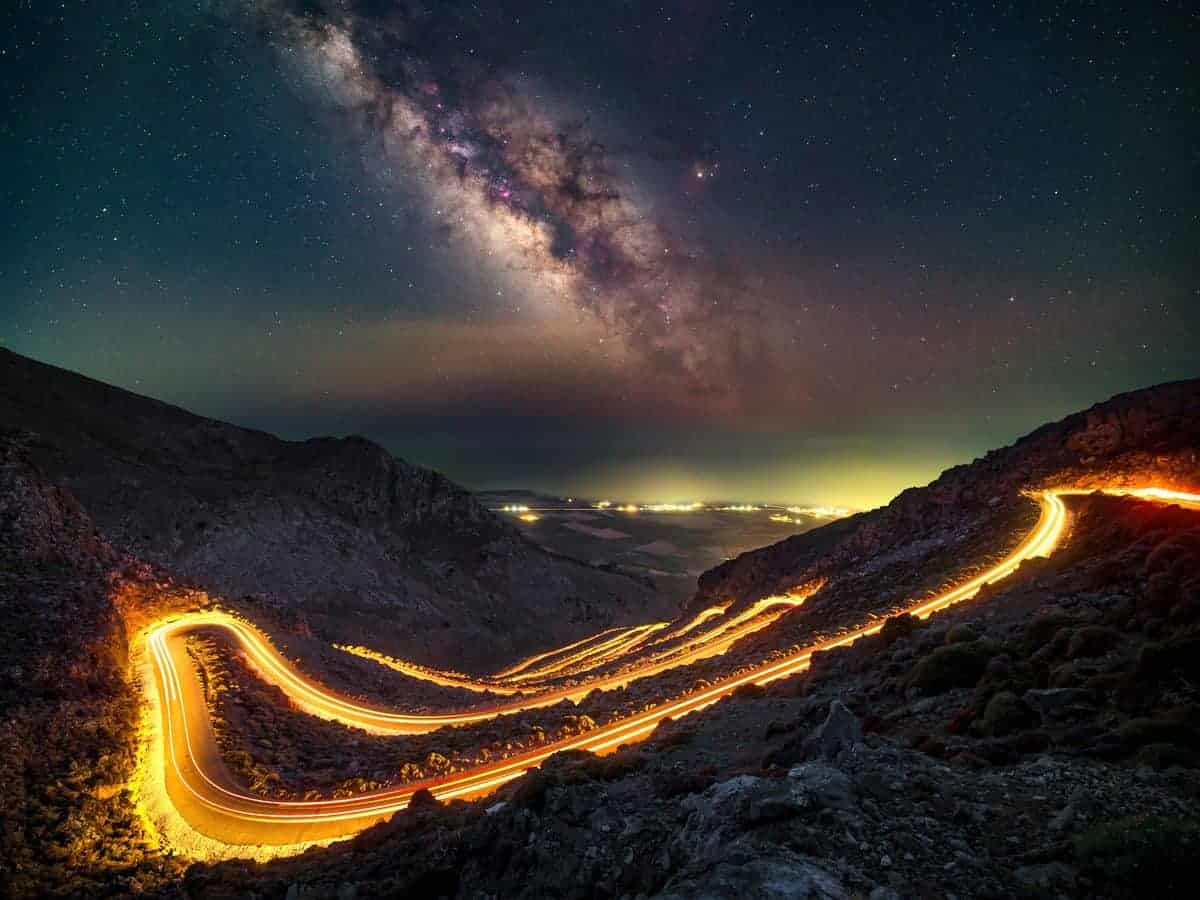 Milky Way over a winding mountain road with car light trails by Evgeni Tcherkasski