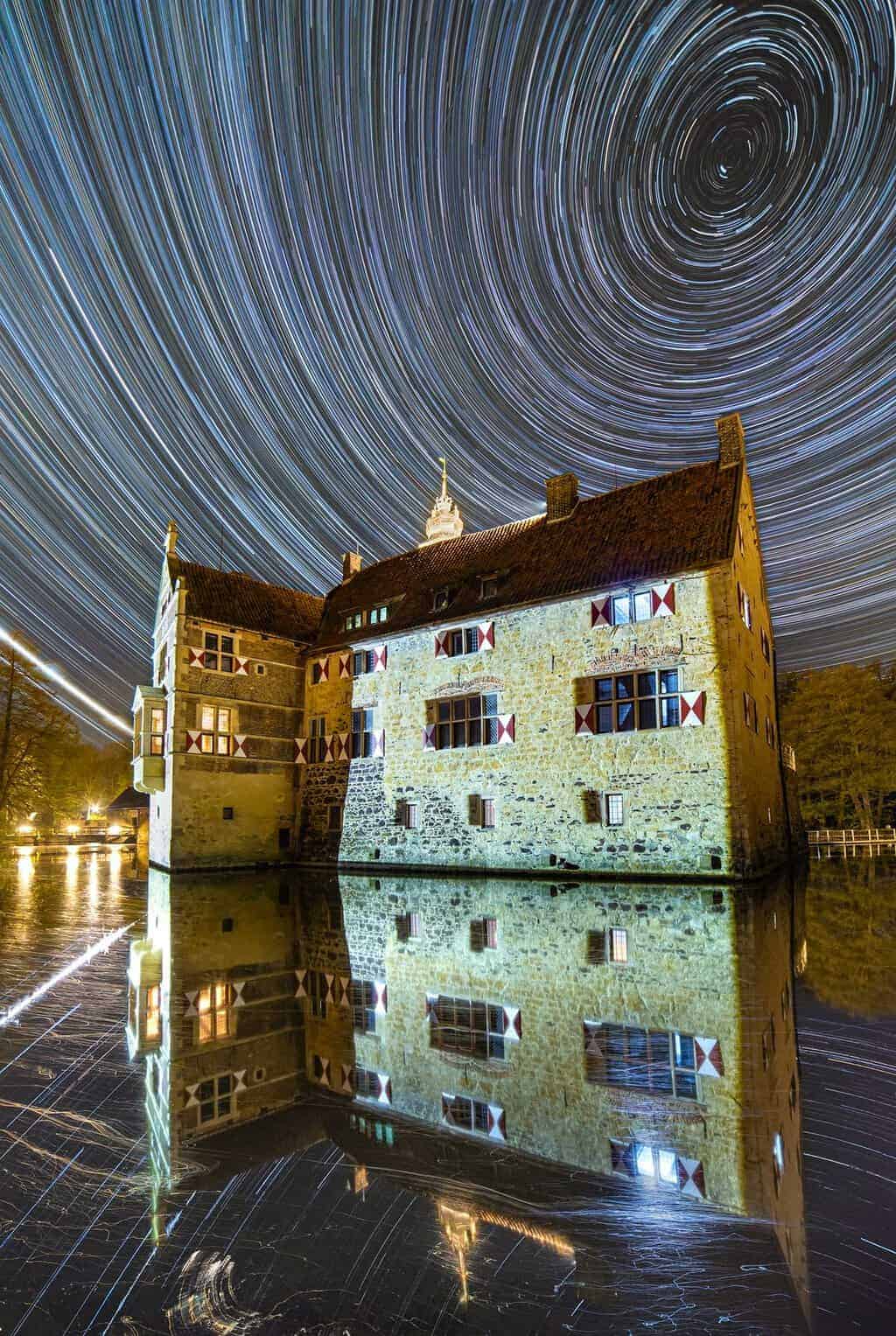 Star trails over a moated castle reflected in water by Evgeni Tcherkasski